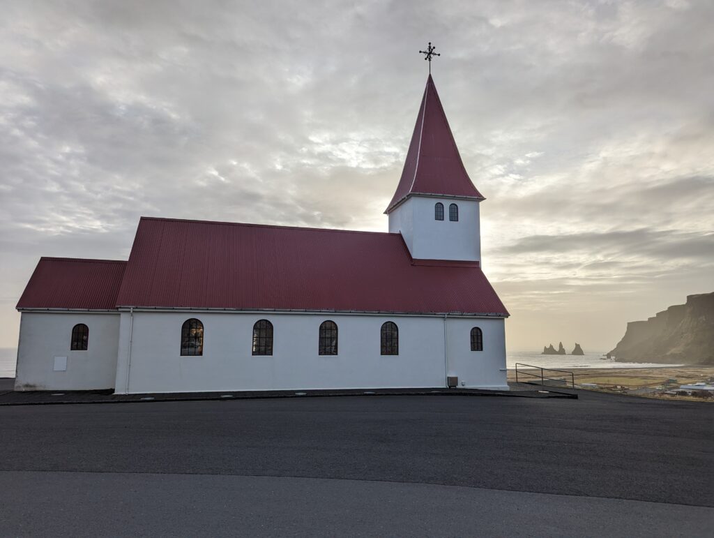 View of the church at Vik with the famous red roof looking towards the stacks in the sea and the black beach