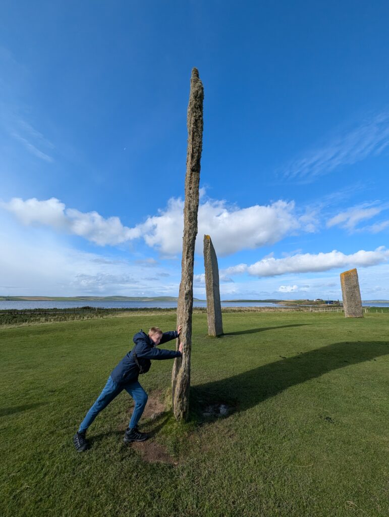 Boy pretending to push a standing stone at Stenness Orkney